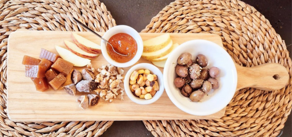 Tabuleiro de madeira com maçã fatiada, compota, frutos secos, doces e azeitonas